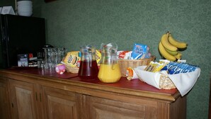 Una encimera de cocina con diversos alimentos y utensilios, incluyendo una licuadora, un cesto de plátanos y una bolsa de papas fritas.