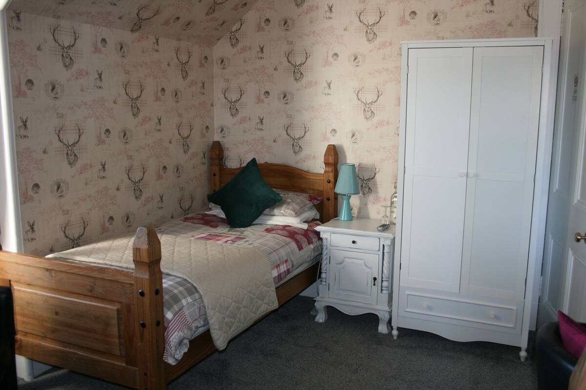 A bedroom with a wooden bed, a nightstand, a white wardrobe, and patterned wallpaper.