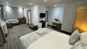 Habitación de hotel con una cama grande, un tocador con espejo, un sofá, un escritorio y un televisor.