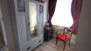 Una habitación con un armario de madera grande, un escritorio de madera pequeño, una silla roja y una ventana con cortinas.