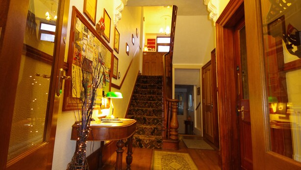 Un pasillo con suelo de madera, un candelabro, cuadros enmarcados y una escalera que sube a otra habitación.