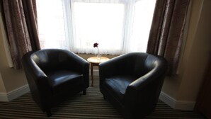 Una habitación con dos sillones de cuero negro, una mesita redonda con un florero y un ventanal con cortinas translúcidas.