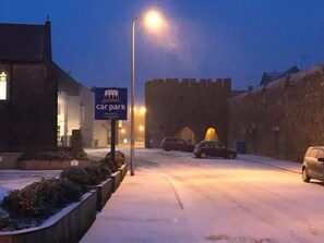 A snowy street with a car park sign, a street lamp, and a building with a turret.
