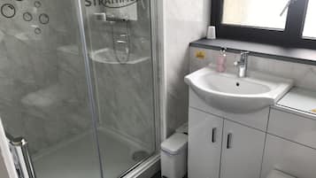 Un baño con cabina de ducha de vidrio identificada con “The Strathmore”, un lavamanos blanco y un espejo sobre él.