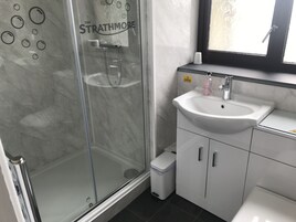 Un baño con cabina de ducha de vidrio identificada con “The Strathmore”, un lavamanos blanco y un espejo sobre él.