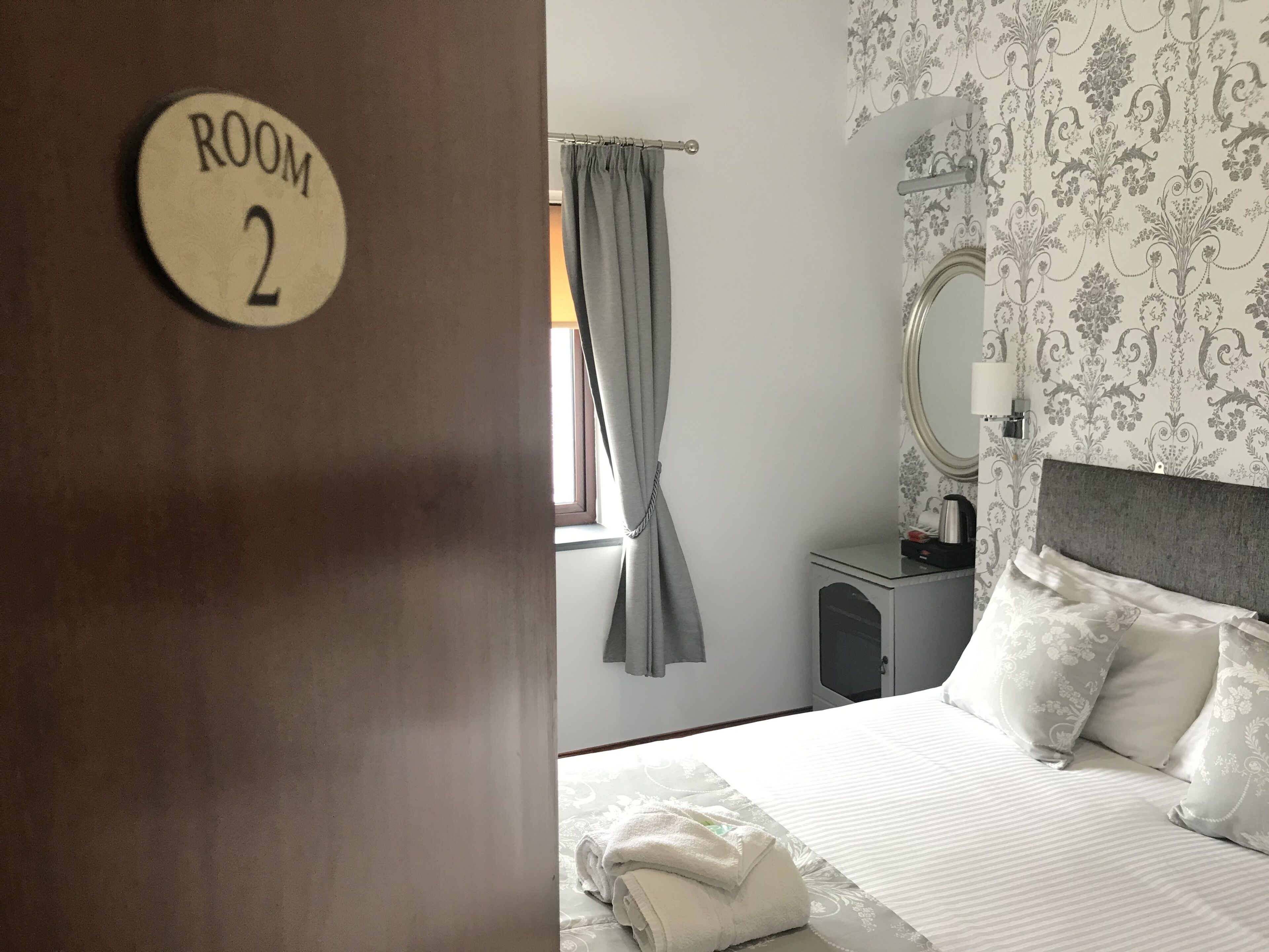 A hotel room with a bed, a bedside table, a mirror, and a curtain.