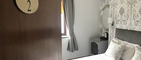 A hotel room with a bed, a bedside table, a mirror, and a curtain.