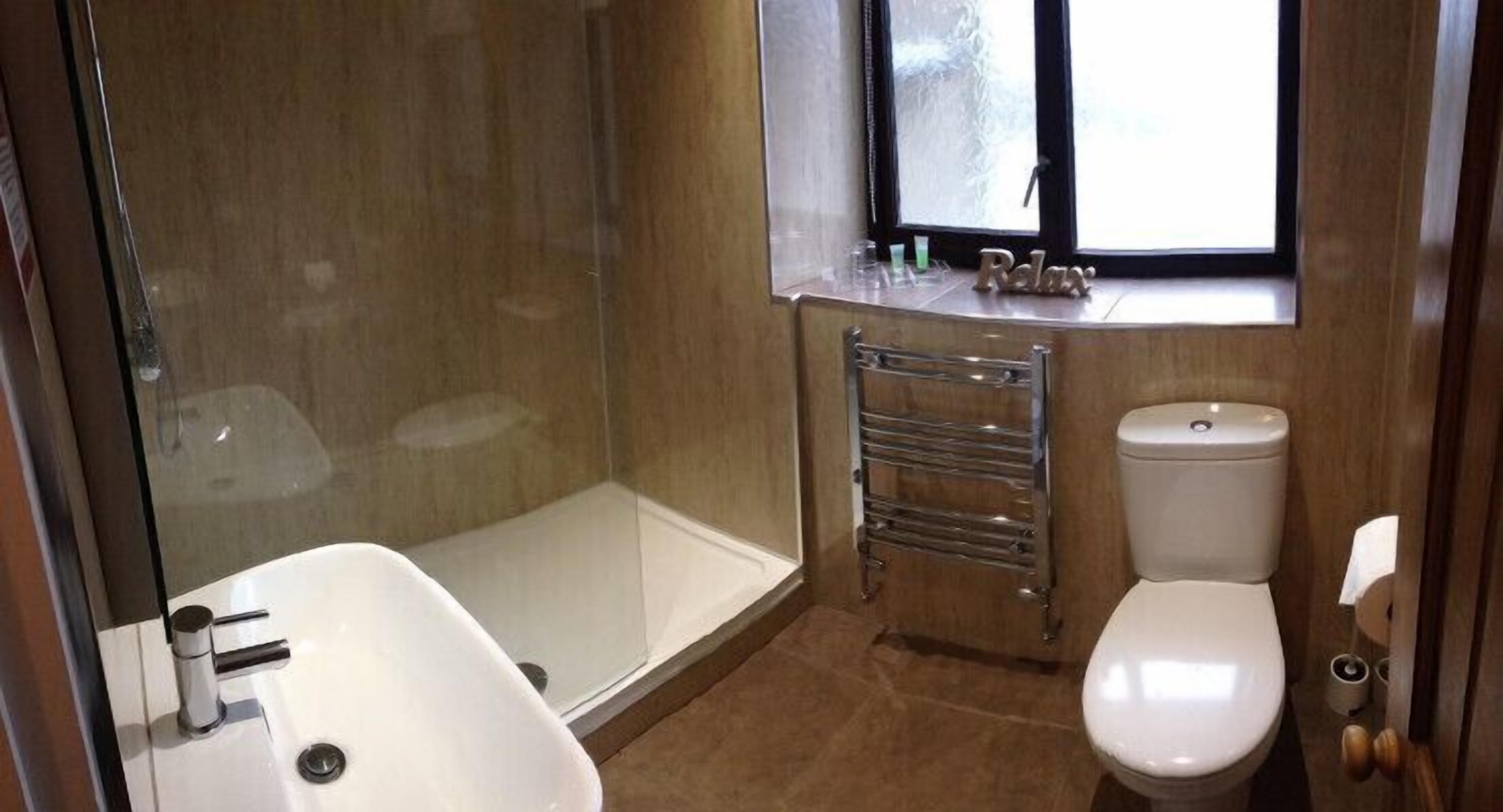 Ein Badezimmer mit Duschkabine aus Glas, einem weißen Waschbecken, einer Toilette und einem Handtuchhalter.