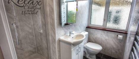 Un baño con puerta de ducha de vidrio, un lavamanos blanco, un inodoro y una ventana con vidrio satinado.