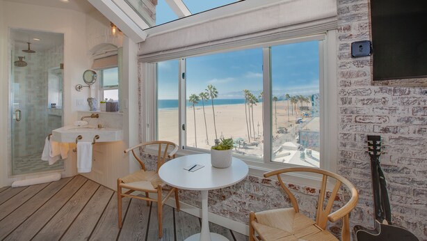 A modern bathroom with a glass shower, a sink with a mirror, and a view of the beach. - Venice V Hotel (Venice)