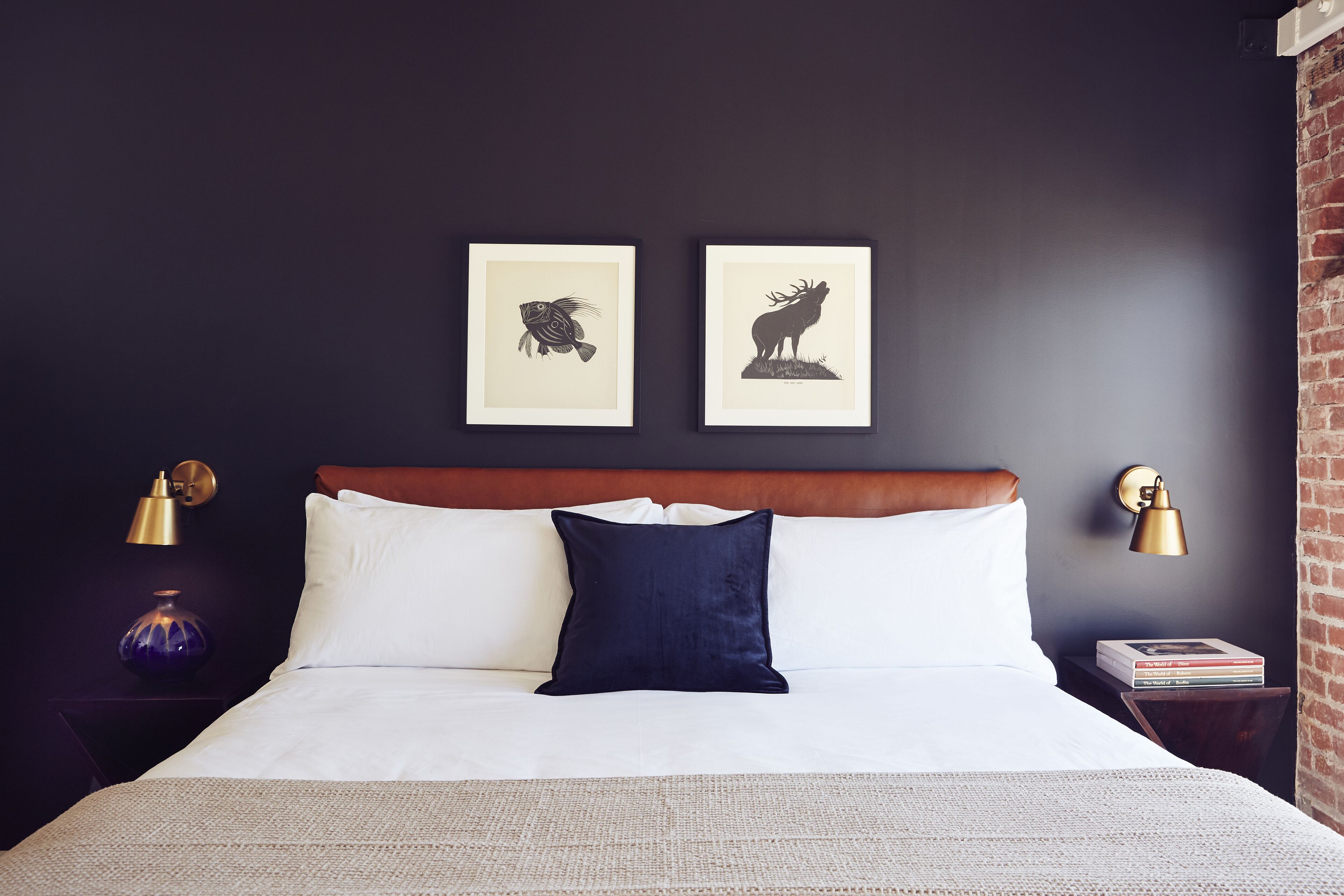 A neatly made bed with white linens and a dark blue pillow, flanked by two framed animal silhouettes on the wall.