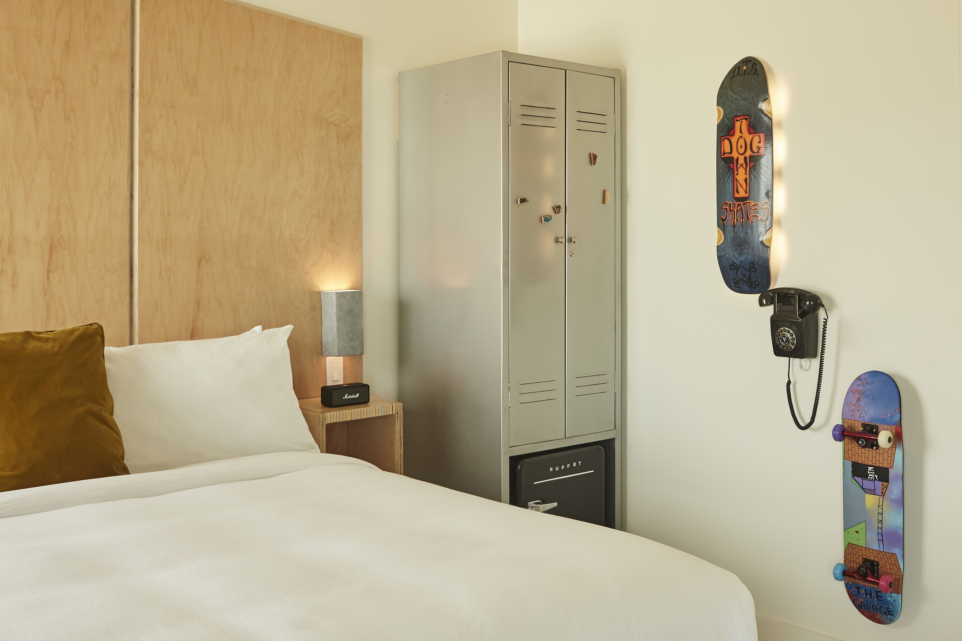 A hotel room with a bed, a wardrobe, a desk with a lamp, and a wall-mounted telephone.