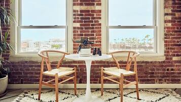 A room with a white table and two wicker chairs, a brick wall, and a view through large windows.