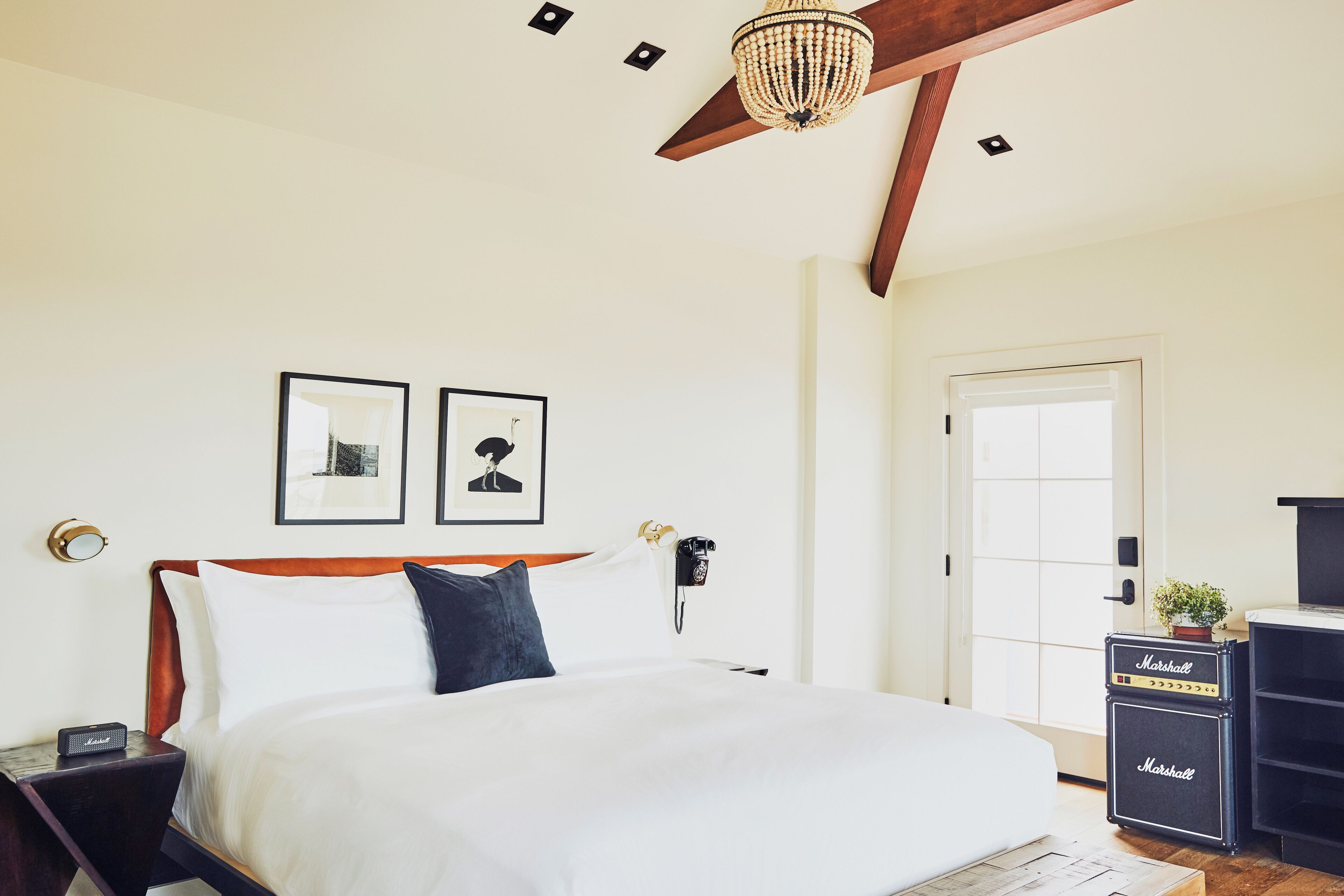 Un dormitorio con cama, candelabro, obras de arte enmarcadas, teléfono y un amplificador Marshall.