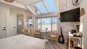 A bedroom with a large bed, a skylight, a TV, a guitar, and a view of the beach. - Venice V Hotel (Venice)