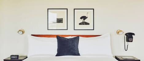 A hotel room with a neatly made bed, two framed pictures on the wall, a bedside telephone, and a small table with a book.