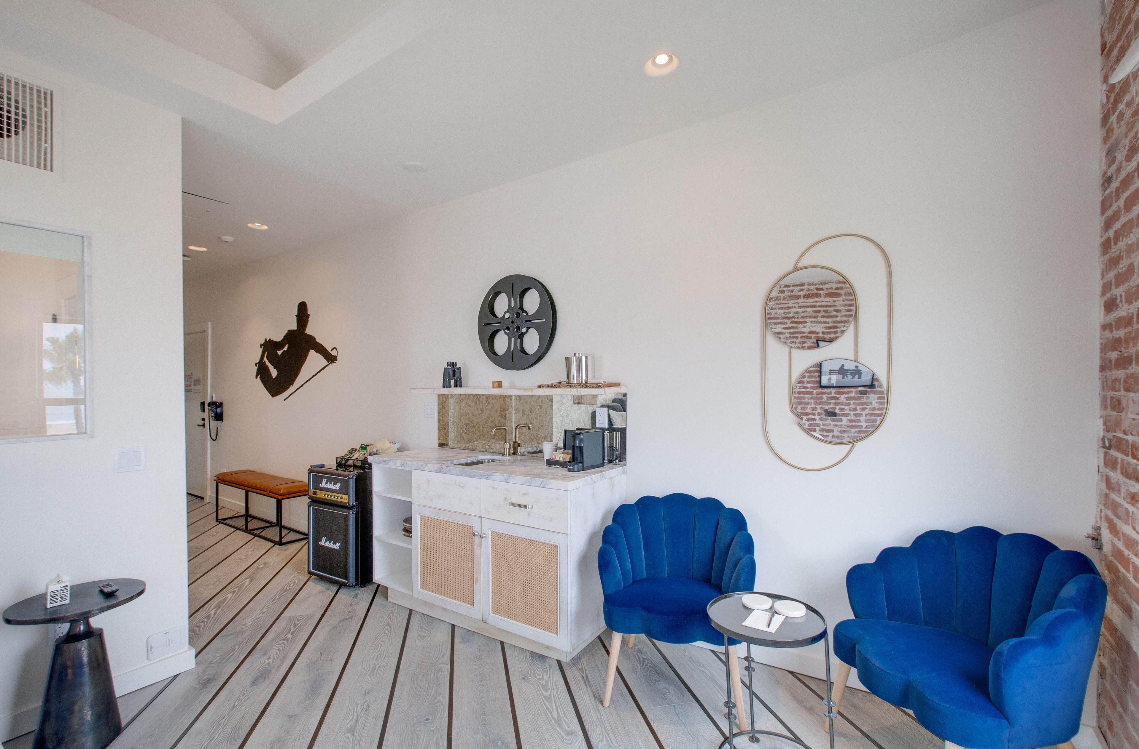 A modern kitchen with a white countertop, a built-in stove, and a coffee machine. There are two blue armchairs and a small round table.