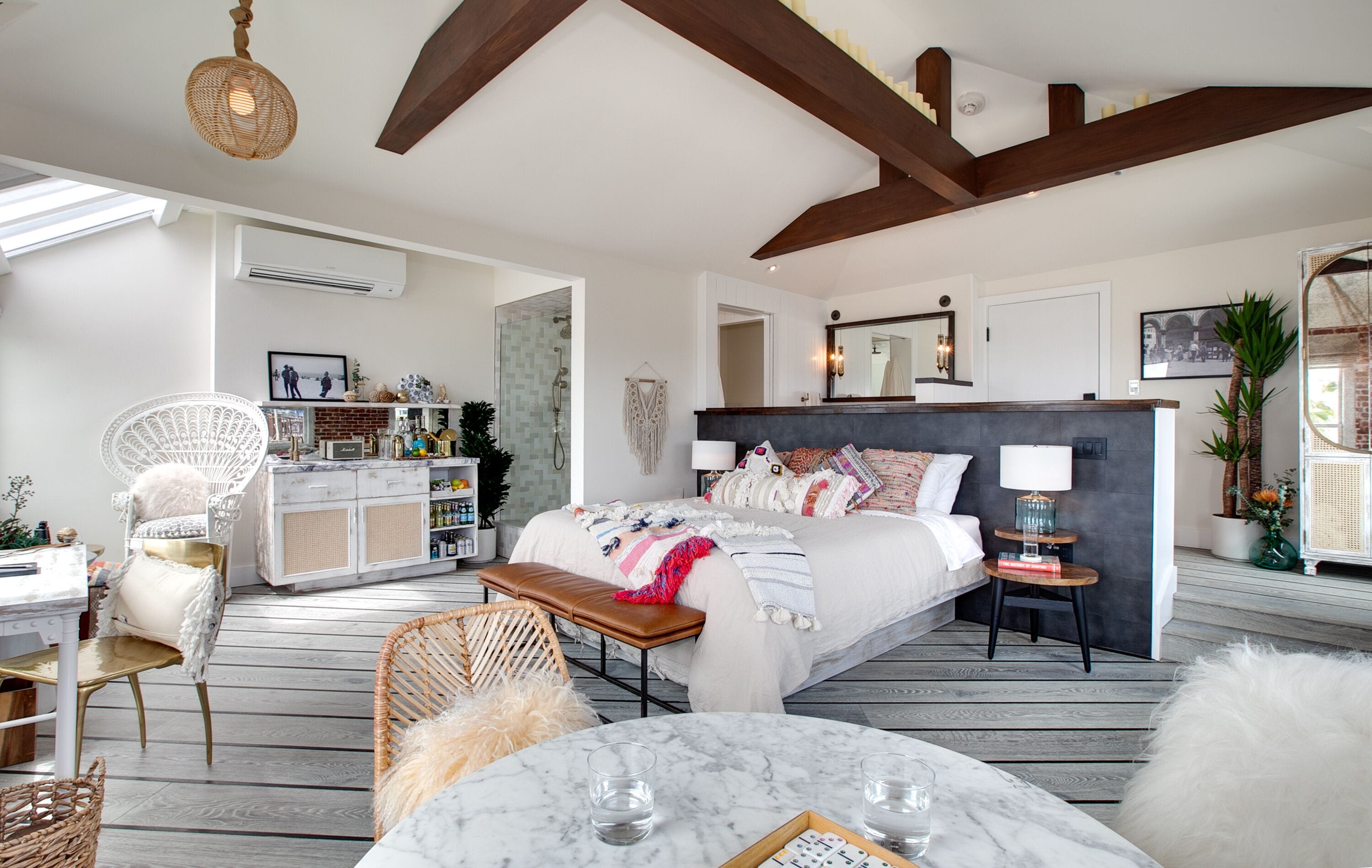 A spacious bedroom with a large bed, bedside tables, a desk, and a chair. There is a window providing natural light and a view of the outside.