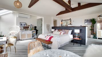 A spacious bedroom with a large bed, bedside tables, a desk, and a chair. There is a window providing natural light and a view of the outside.