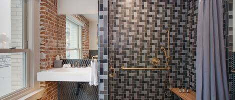 A modern bathroom with a brick wall, a large window, a shower with a glass door, and a sink with a towel rack.