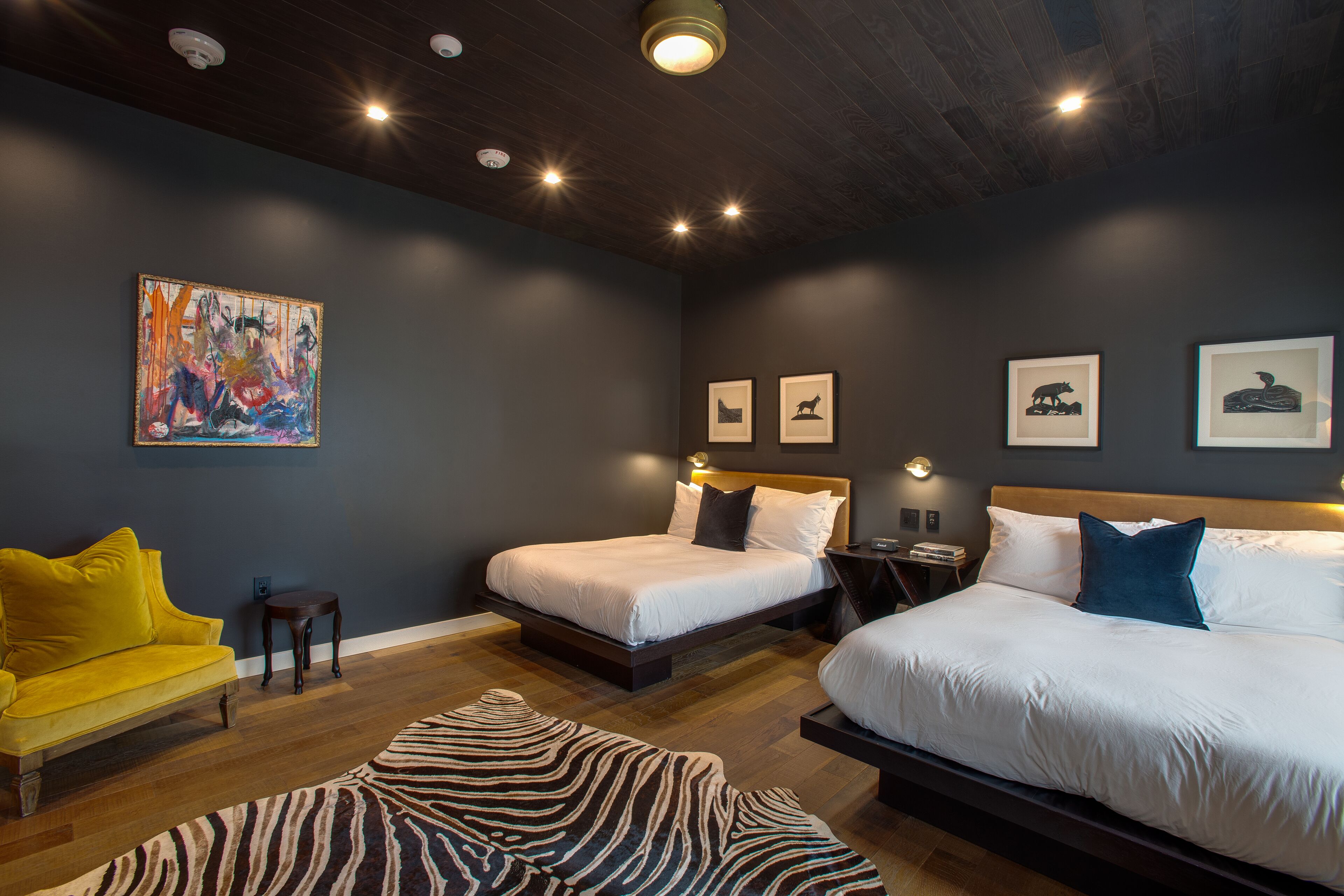 Quarto moderno com duas camas, um tapete com padrão de zebra e um quadro abstrato colorido na parede.