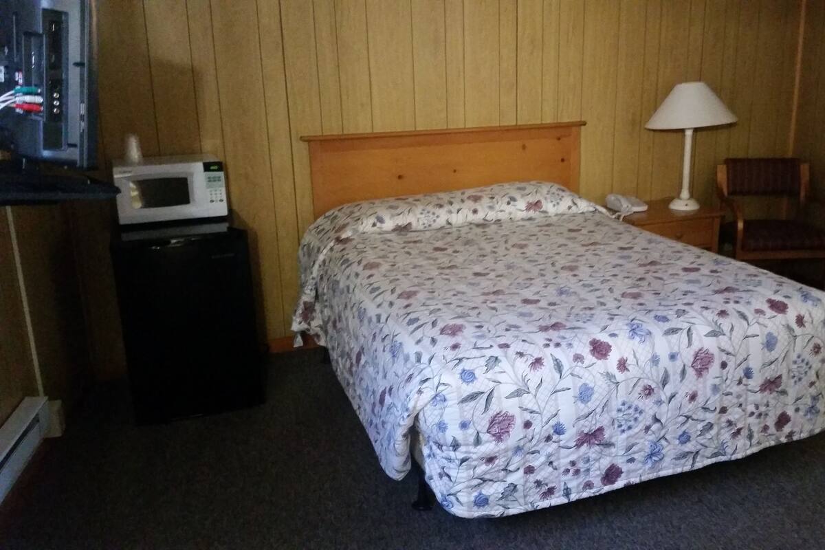 A single bed with a floral bedspread, a nightstand with a lamp, a telephone, and a microwave on a small table.