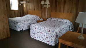 Una habitació amb dos llits, un escriptori de fusta i una tauleta de nit amb una làmpada.