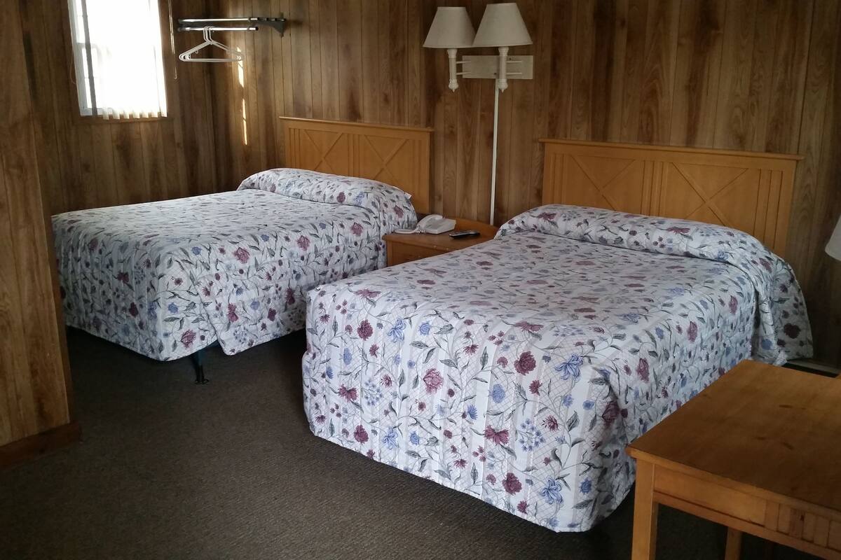 A room with two beds, a wooden desk, and a nightstand with a lamp.