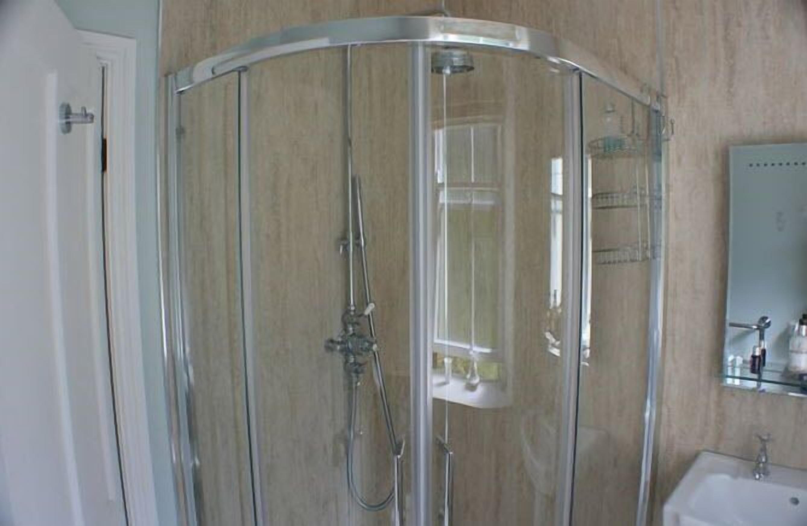 A glass-enclosed shower stall with a handheld showerhead and a wall-mounted faucet.