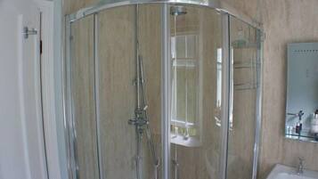 A glass-enclosed shower stall with a handheld showerhead and a wall-mounted faucet.