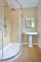 Un baño con ducha acristalada, lavabo pedestal y espejo sobre él.
