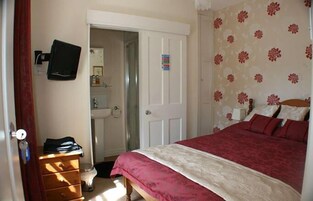 Un dormitorio con cama, cómoda, televisor y puerta que da al baño.