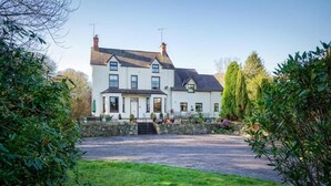 A large, two-story house with a stone facade, a front porch, and a driveway leading to a grassy area. - Craig Y Glyn (Pwllheli)