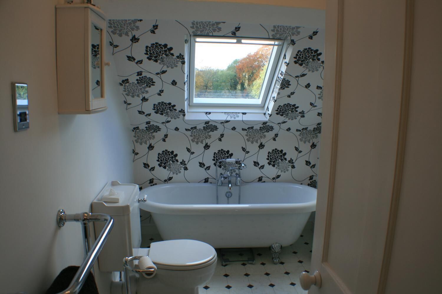 Een badkamer met een vrijstaand bad, een toilet en een raam boven de wastafel.