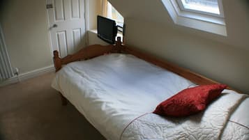 A single bed with a red pillow, a TV mounted on the wall, and a skylight above.