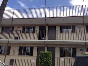 Un edificio de varios pisos con techo plano, un balcón en el segundo piso y una señal de salida de incendios en la pared exterior.