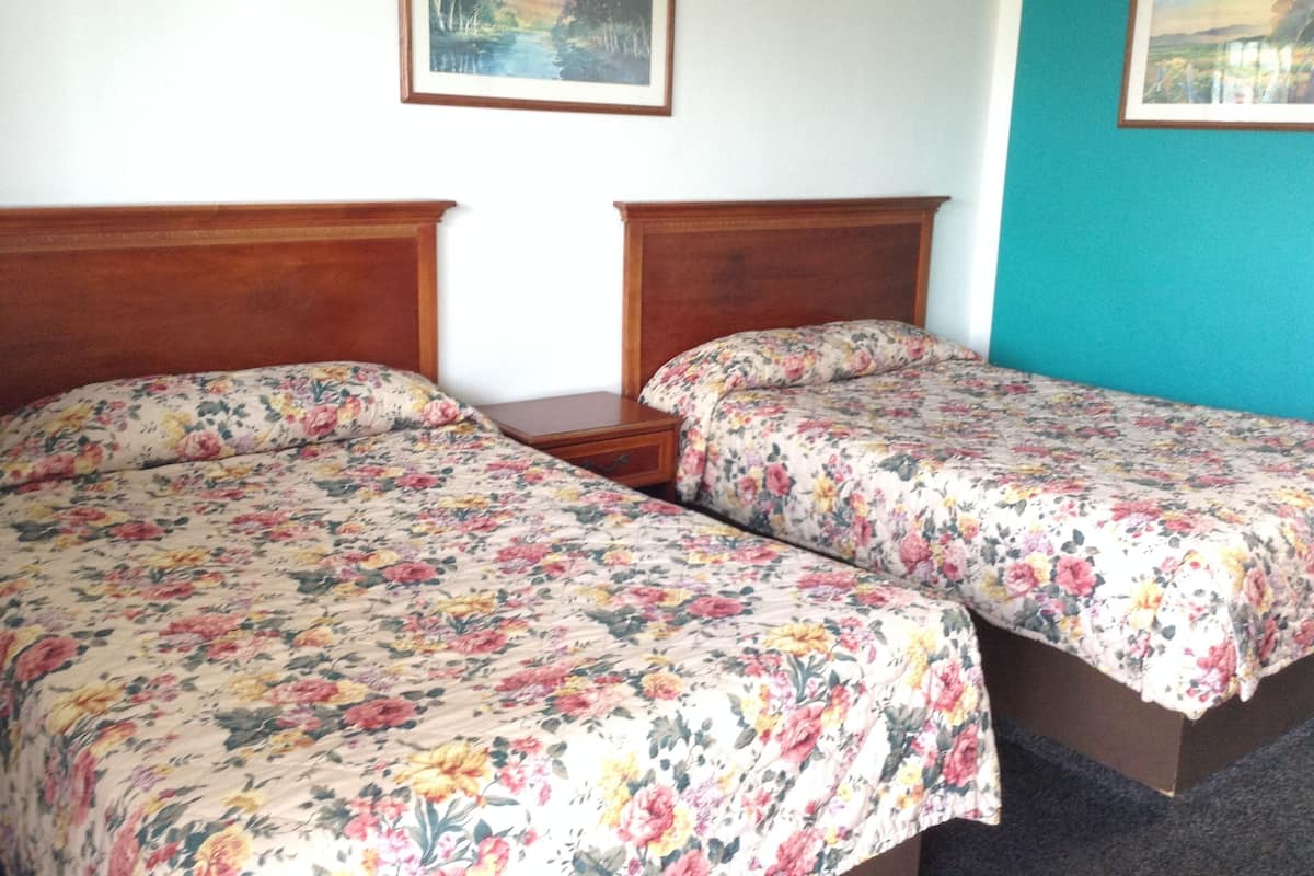 Ein Zimmer mit zwei Holzbetten, floralem Bettzeug, einem kleinen Nachttisch und einem gerahmten Gemälde an der Wand.