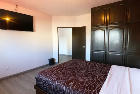 Un dormitorio con cama, armario, televisor y puerta que da a otra habitación.