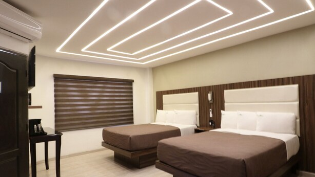 A modern hotel room with two beds, a wooden headboard, a flat-screen TV, a coffee maker, and a window with blinds. - Hotel Bugambilias (Ensenada)