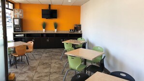 A restaurant interior with orange walls, a flat-screen TV mounted above the counter, and several tables and chairs. - Hotel Bugambilias (Ensenada)
