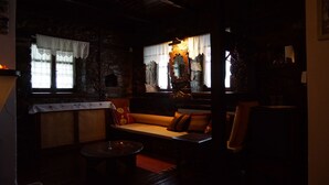 Una habitación tenuemente iluminada con una pared de piedra, un banco de madera y una mesa con una vela.