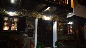 Un edificio de piedra con puerta de madera oscura, plantas en macetas y un letrero.