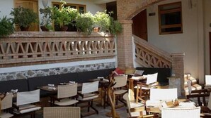 Un espacio al aire libre cubierto con varias mesas y sillas, una pared de ladrillo con un diseño decorativo y plantas en macetas.