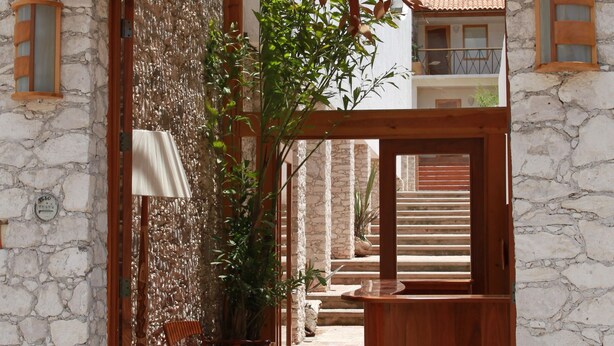 Un edificio de piedra con un arco de madera que da a un patio interior. Hay sillas y una mesa en el patio, y se observa una escalera al fondo.
