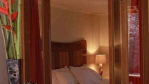 Una habitación de hotel con cama, mesita de noche, lámpara y una silla de madera.