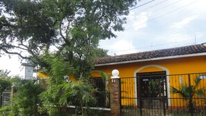 A yellow building with a black gate, surrounded by greenery and a paved sidewalk. - Hotel Casa Barcelona (Granada)