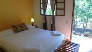 A bed with a white comforter, a patterned pillow, and a folded white towel. There is a nightstand with a lamp and a window with curtains. - Hotel Casa Barcelona (Granada)
