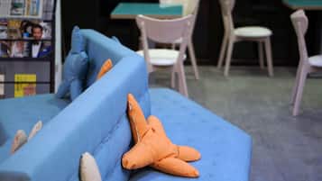 Ein blaues Sofa mit orangefarbenen und beigefarbenen Kissen in einem Raum mit Tisch und Stühlen.