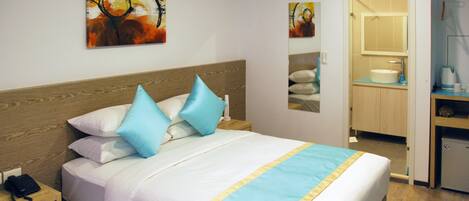 A hotel room with a bed, a nightstand, a desk, and a bathroom visible through an open door.