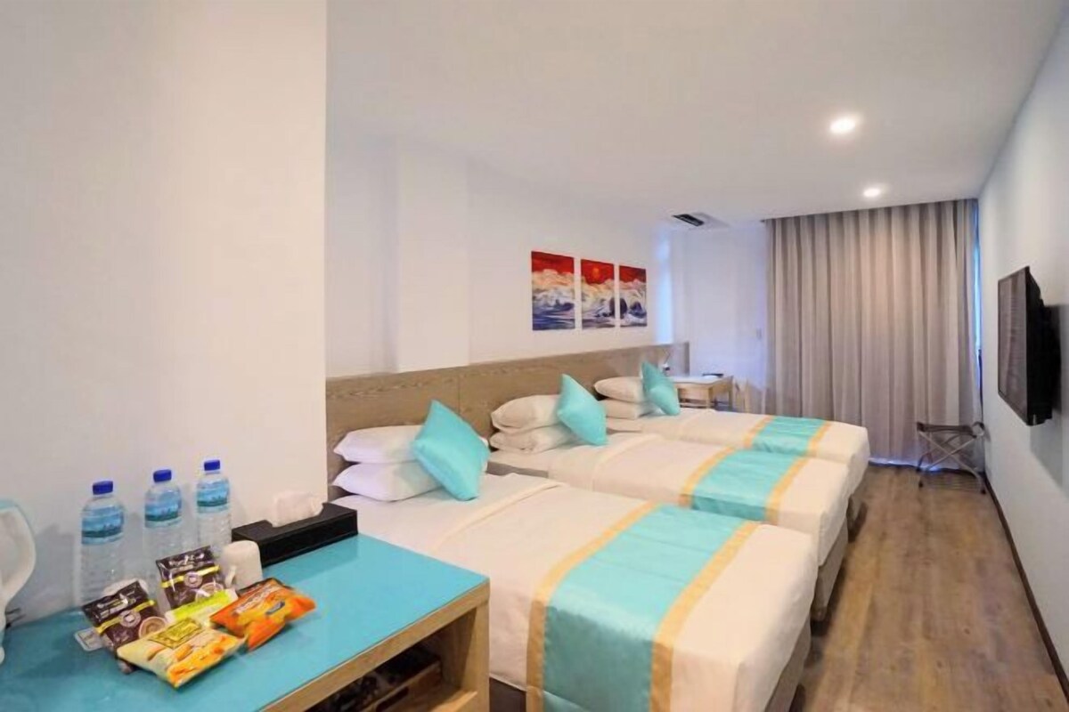 A hotel room with two beds, a desk with snacks, a TV, and a window with curtains.